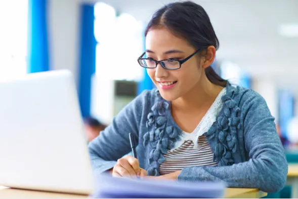 Bimbel OSN Matematika Exademy, siswi SMA berkacamata menulis catatan dengan laptop di meja